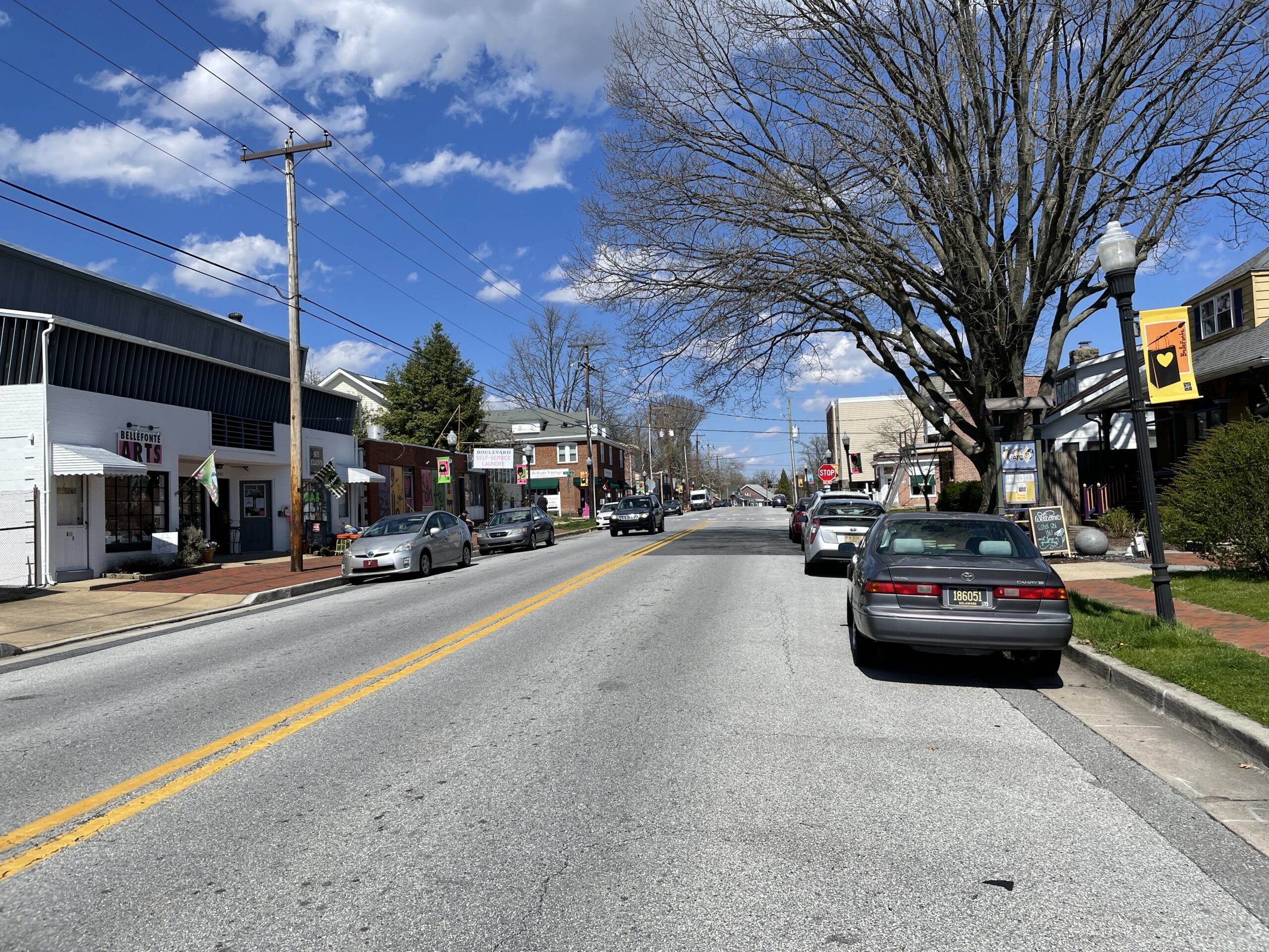 Brandywine Boulevard in Bellefonte, DE, showing a quiet street with parked cars, local shops, and trees lining the sidewalk under a clear blue sky."