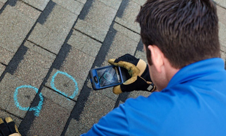 Roof inspector photographing hail damage on shingle roof, assessing roof condition after a storm