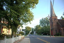 A quiet street in the historic district of Laurel, DE, featuring charming homes with white picket fences and a tall brick church steeple. G. Fedale, top roofing and siding experts in Laurel, DE.