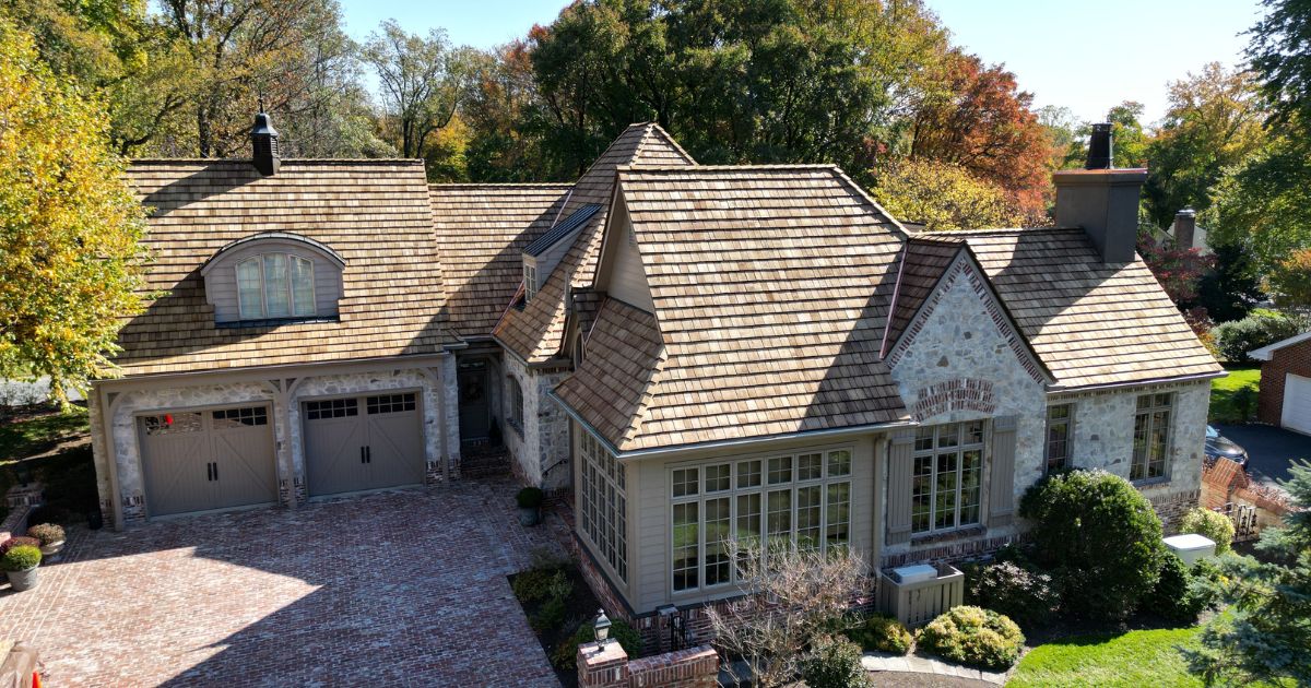 A stunning residential home featuring a cedar shake roof with intricate design, surrounded by lush landscaping and vibrant autumn foliage.